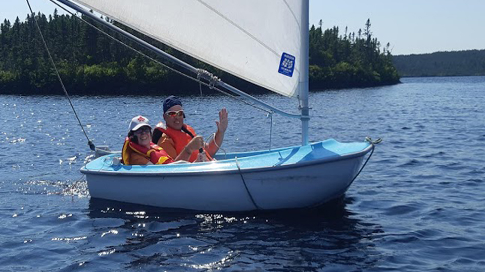two young people in sailboat waving and smiling